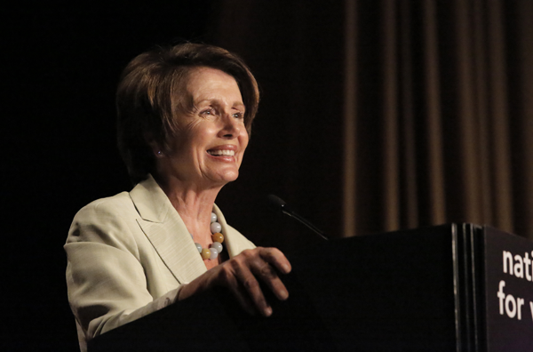 Nancy Pelosi smiling, speaking at a podium