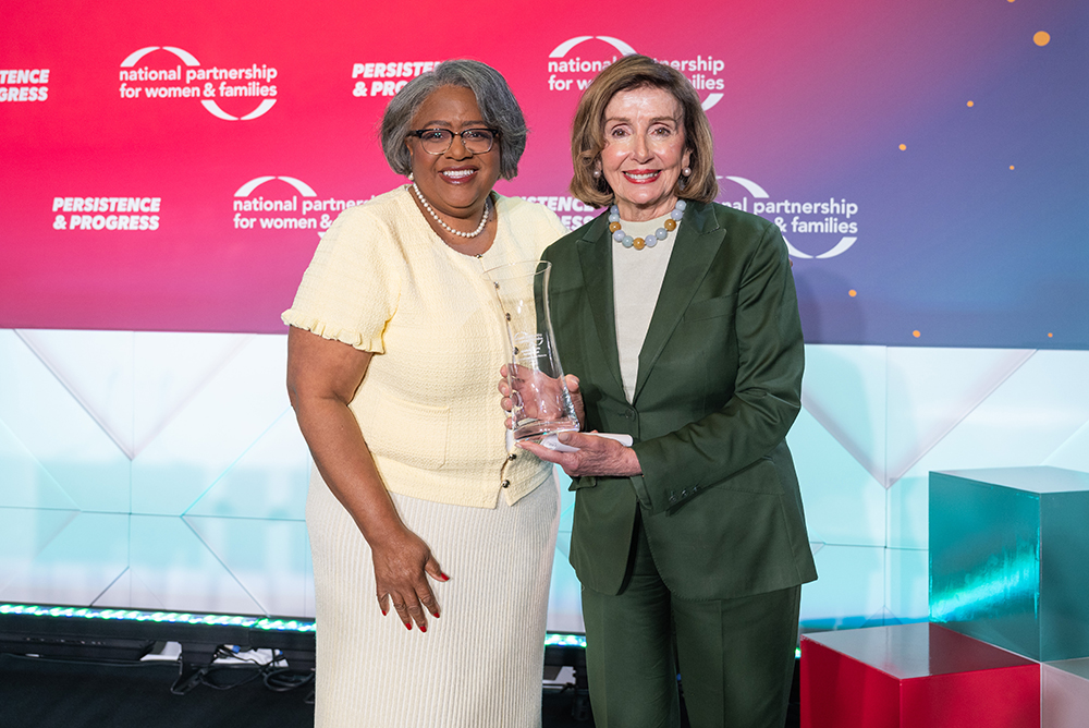 NPWF President Jocelyn Frye and Speaker Emerita Nancy Pelosi holding a glass vase award on stage at the 2026 Annual Event