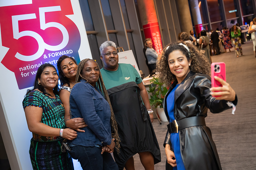 A group of attendees taking a selfie photo in front of a sign that reads 55 & Forward at the 2026 Annual Event