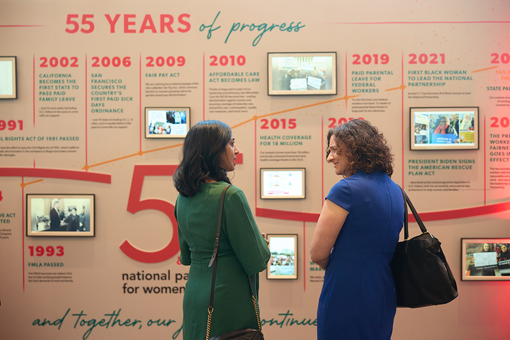 Two attendees talking in front of the interactive timeline exhibit wall at the 2026 Annual Event