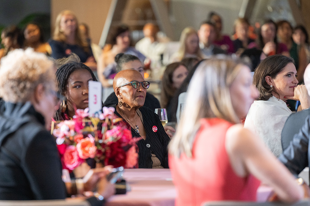 Attendees sitting at a table listening to an honoree with other attendees in the background at the 2026 Annual Event