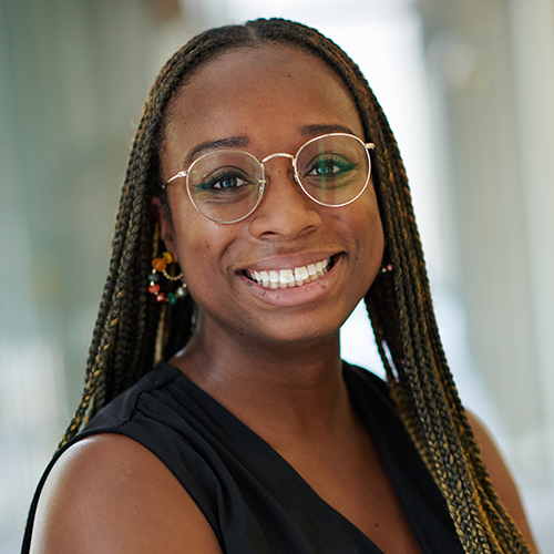 Amani Echols, the senior manager of maternal & infant health. She is a young Black woman with long braided hair. She is smiling, wearing a black sleeveless blouse, silver thin wired eyeglasses and colorful earrings with red, orange, green, and gold beads.