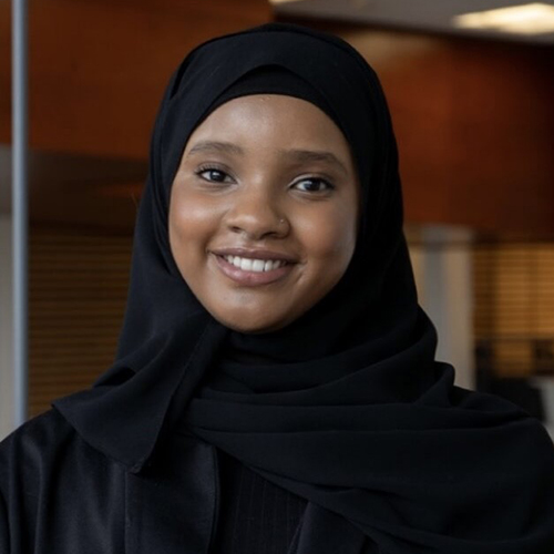 Portrait photo of Hodan Deria. She is a young Black woman, smiling in the photo, wearing a black hijab with a black dress.