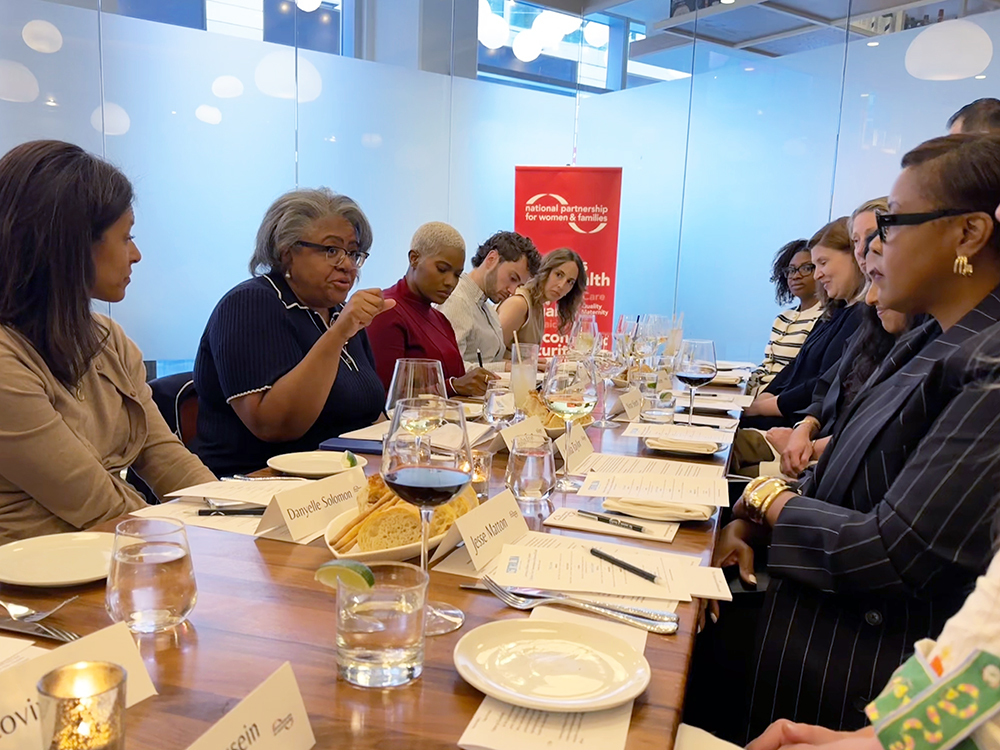 A mother's day conversation with policy experts, nonprofit and business leaders hosted by the National Partnership in May 2026. 10 participants are sitting around a long wood dining table with plates, silverware, drinking and wine glasses in front of each person.