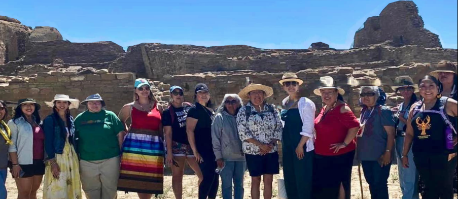 A group of Native woman standing and smiling at the camera, huddled for a group photo